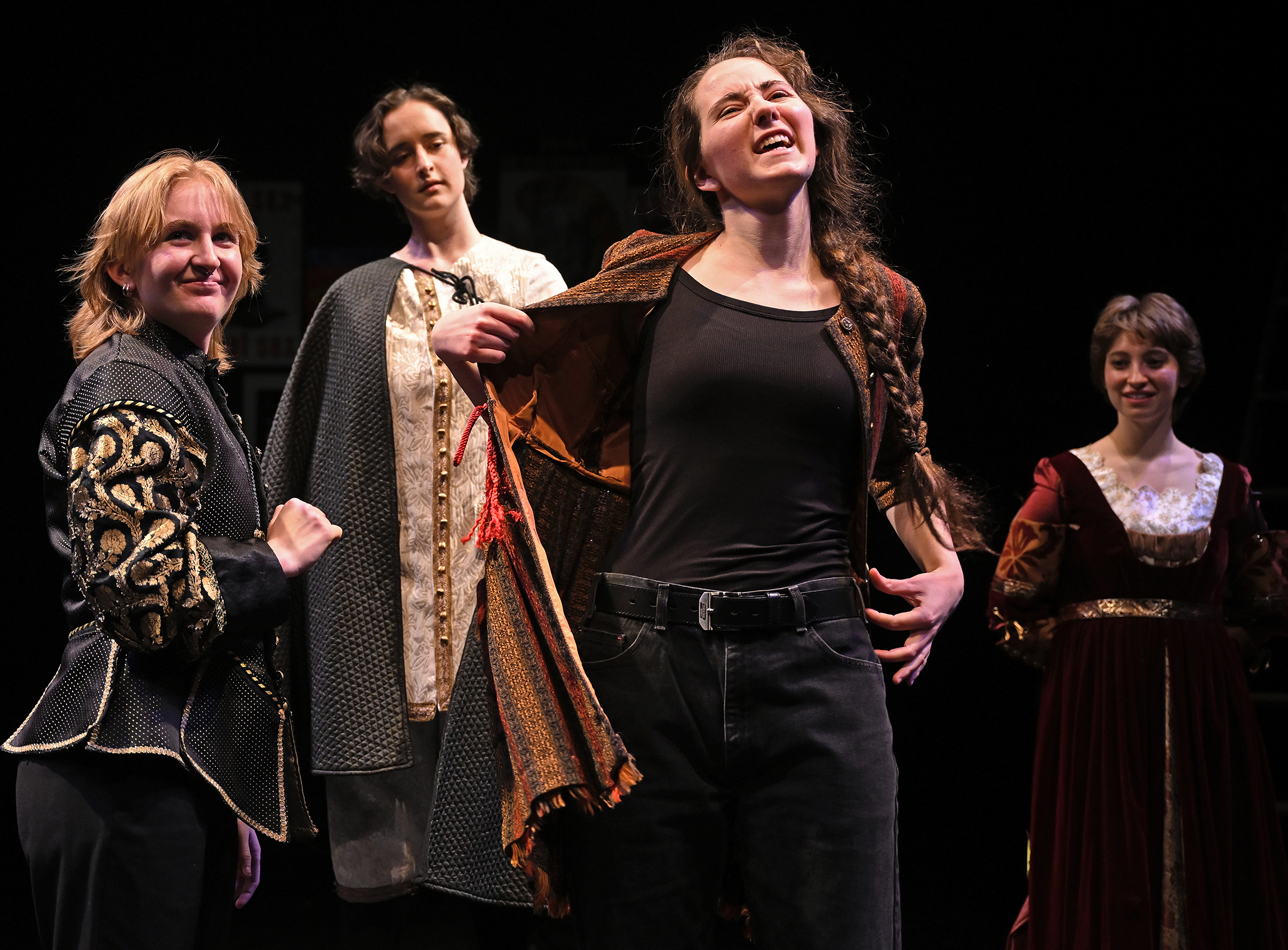 An actor on stage removes their jacket surrounded by other characters in the play