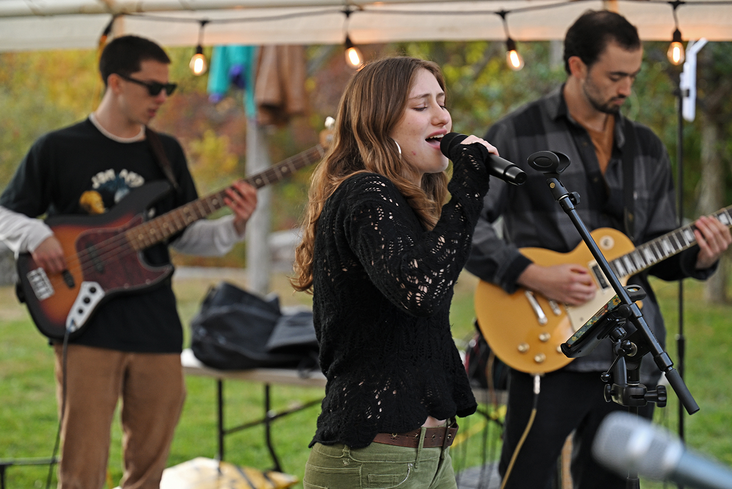 A singer and two guitarists perform at an outdoor rock concert.