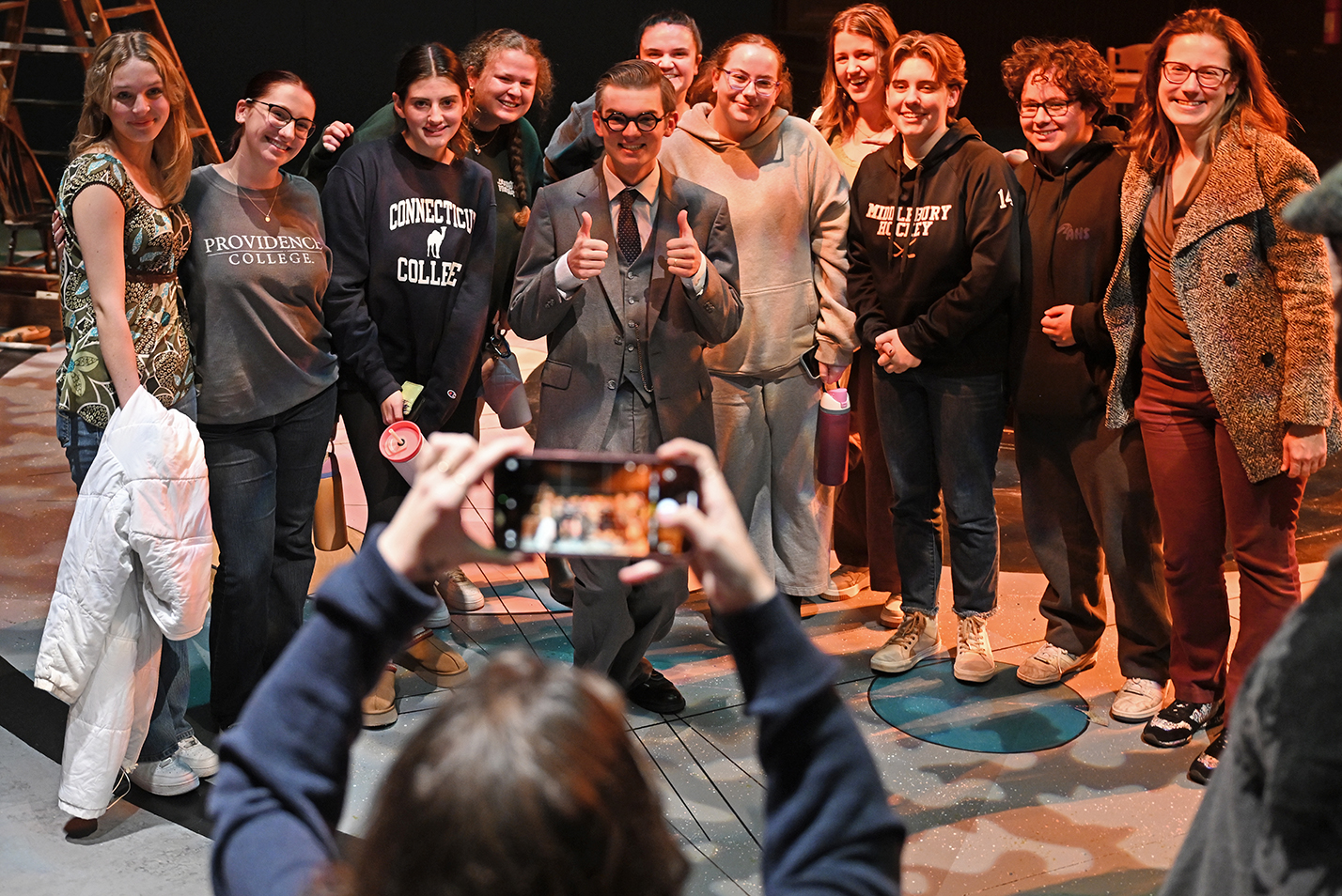 A group of actors gather for a photo as one holds two thumbs up after performing a play in a black box theater.